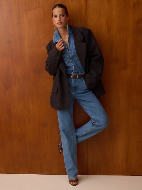 Model in dunklem Blazer und Jeans vor einer Holzwand